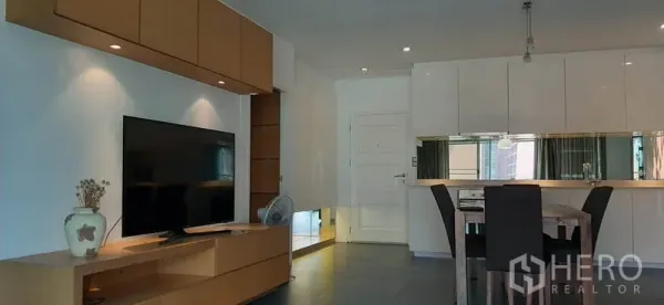 Condominium for rent in Phaya Thai, Bangkok - Living area with large TV, built-in cabinets and a dining table beside the glossy kitchen.