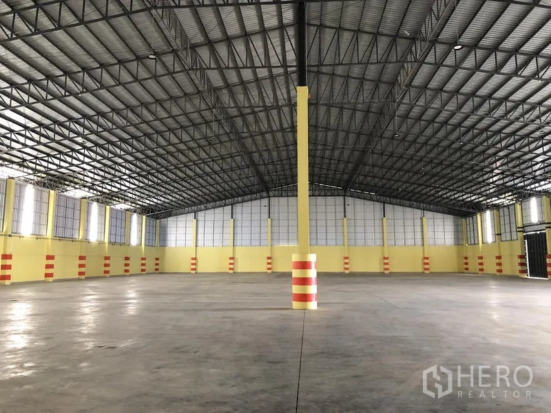 Warehouse for rent in Phra Nakhon Si Ayutthaya - Empty open-span warehouse with high steel roof, bright yellow walls and smooth concrete floor.