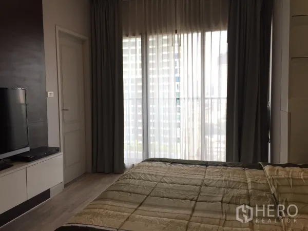 Condominium for rent or sale in Bangkok - Bedroom with floor-to-ceiling curtains opening to a balcony and city view.