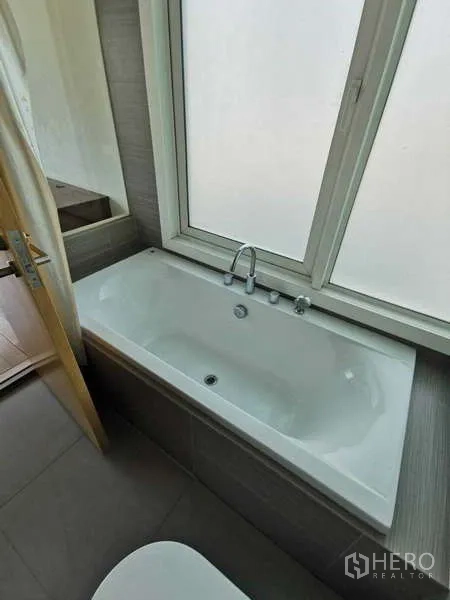 Condominium for rent in Khlong Toei, Bangkok - Bathroom featuring a soaking bathtub beneath a frosted window.
