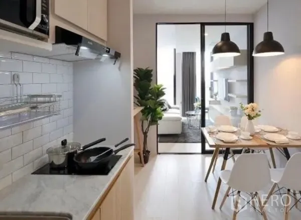 Condominium for rent in Pathum Wan, Bangkok - Modern galley kitchen with white subway tiles, induction hob, and a dining table under pendant lights.
