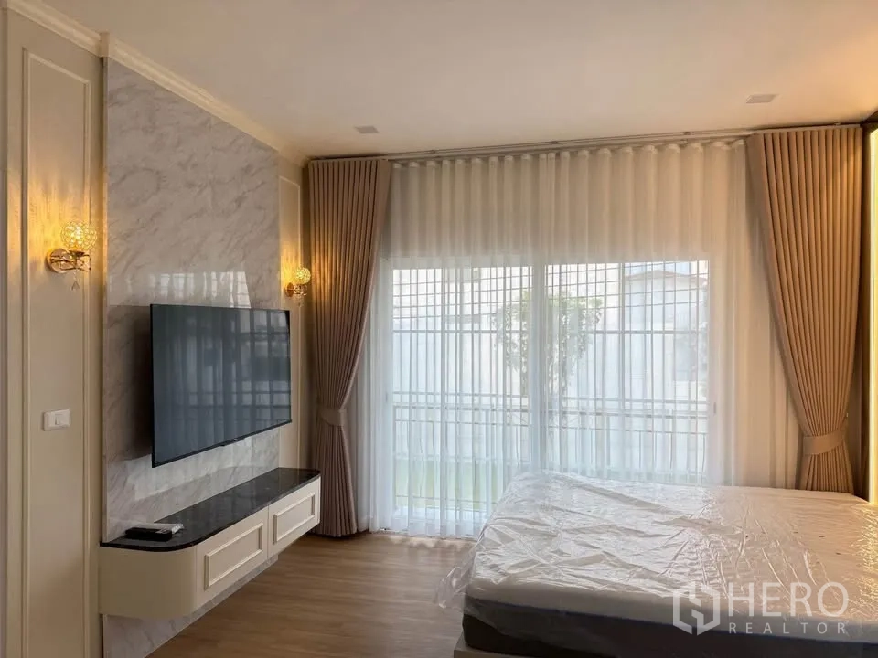 Semi-detached House for rent in Mueang Samut Prakan, Samut Prakan - Bedroom view with wall-mounted TV, marble accent wall, and sheer curtains.