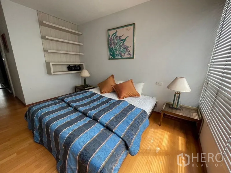 Condominium for sale in Khlong Toei, Bangkok - Cozy bedroom with double bed, bedside tables and wall shelves by large window blinds.