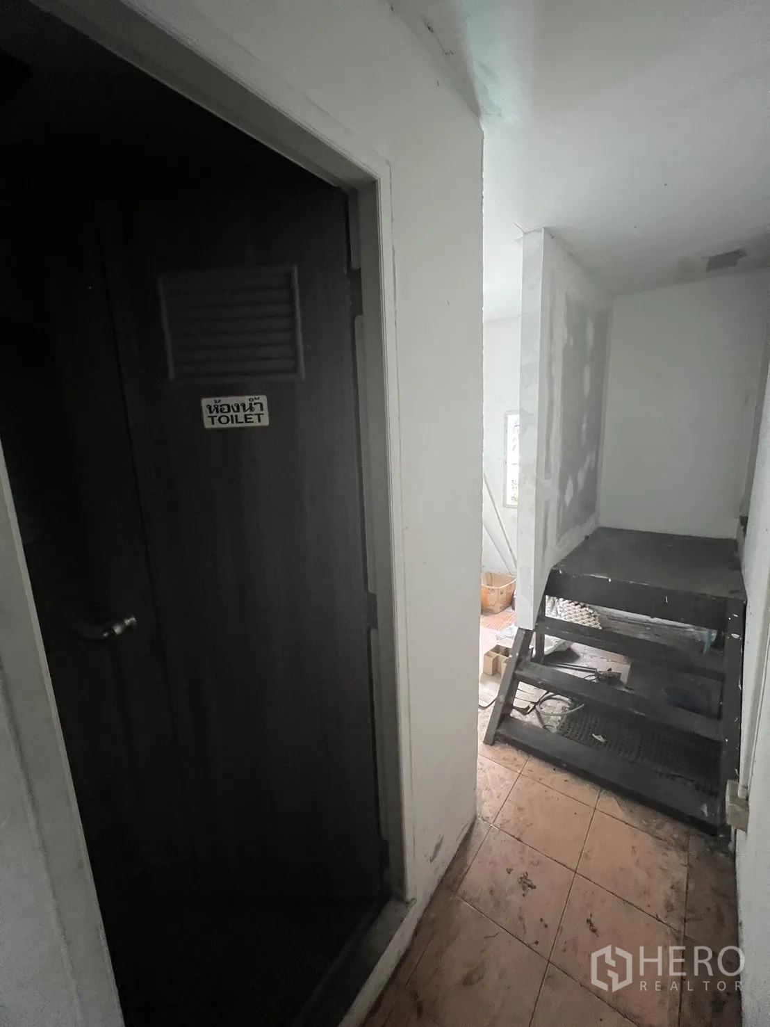Shophouse for rent in Khlong Toei, Bangkok - Upper-floor corridor with a toilet door and metal service stairs beside tiled flooring.