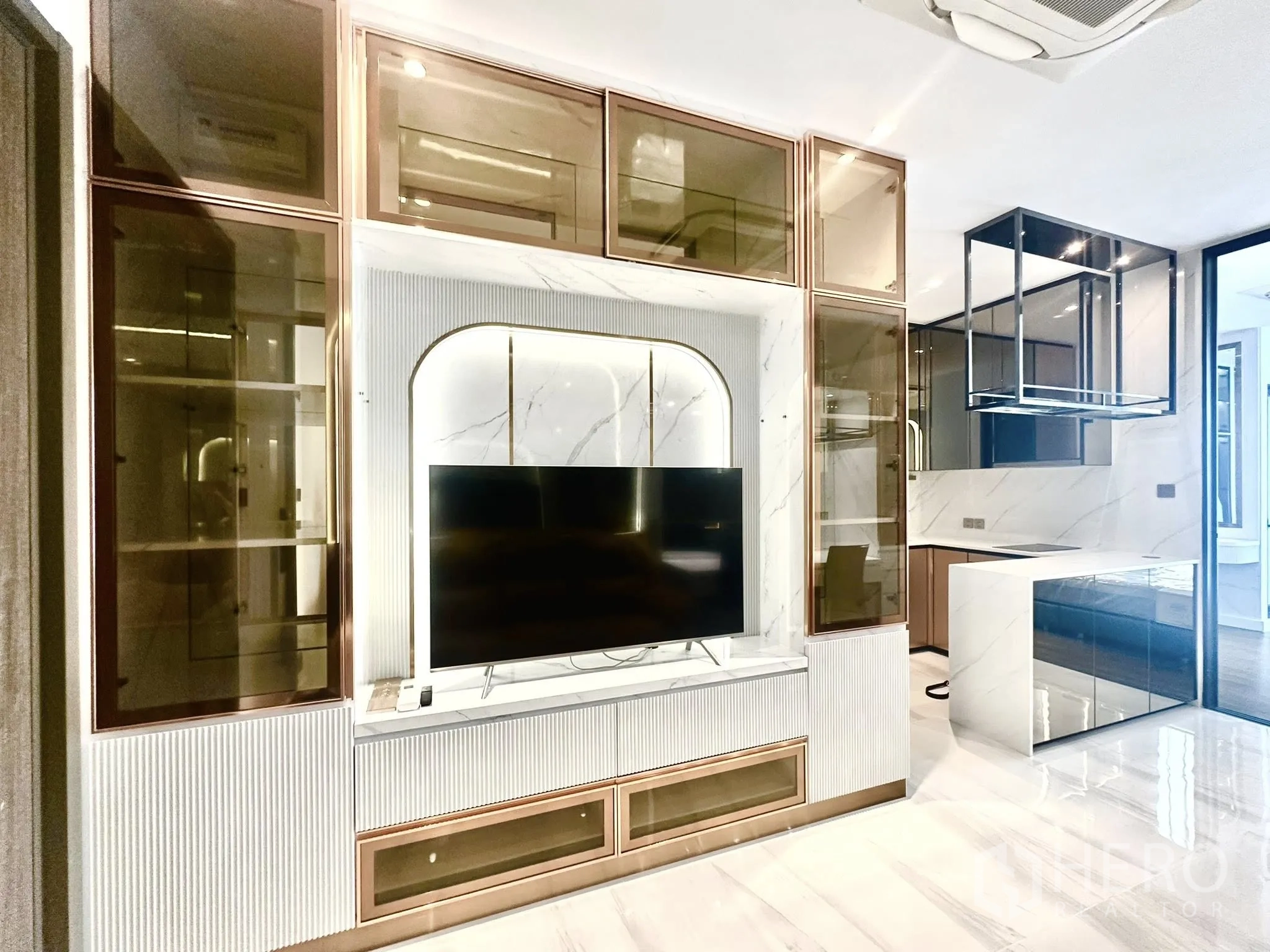 公寓 for rent in Sathon, Bangkok - 内置电视墙搭配玻璃柜体，旁为简洁的厨房岛台。