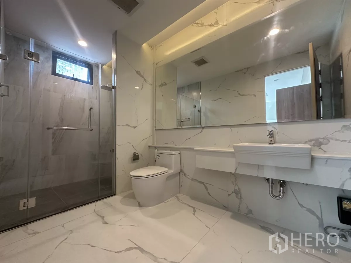 Townhouse for rent in Watthana, Bangkok - Covered carport with tiled floor, two wooden doors, and an EV charging point.