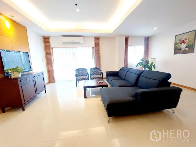 Apartment for rent - Airy lounge with L-shaped sofa, TV cabinet, two armchairs and large windows with blinds.
