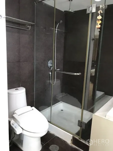 公寓 出租在Watthana, Bangkok - 现代化浴室，玻璃淋浴房与坐便器，深色瓷砖墙面。