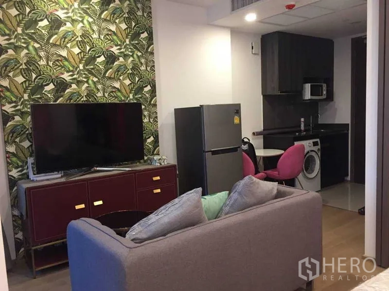 Condominium for rent in Bang Rak, Bangkok - Open-plan living with tropical feature wall, TV console, fridge and kitchenette.