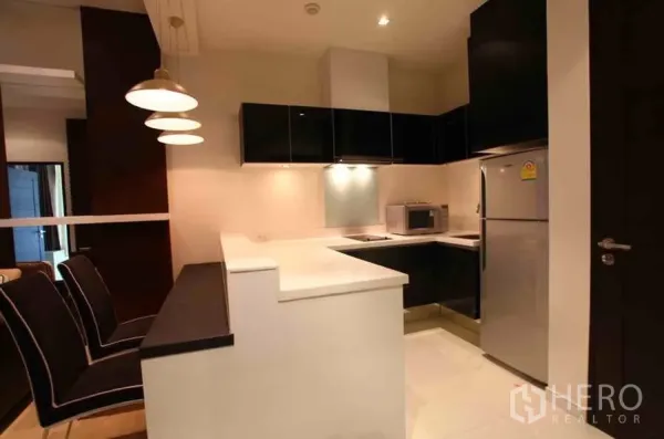 公寓 出租在Watthana, Bangkok - 现代U型厨房，亮面橱柜、吧台、冰箱与微波炉，灯光充足。