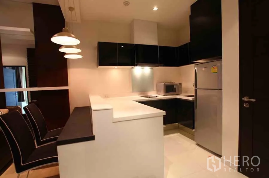 公寓 出租在Watthana, Bangkok - 现代U型厨房，亮面橱柜、吧台、冰箱与微波炉，灯光充足。