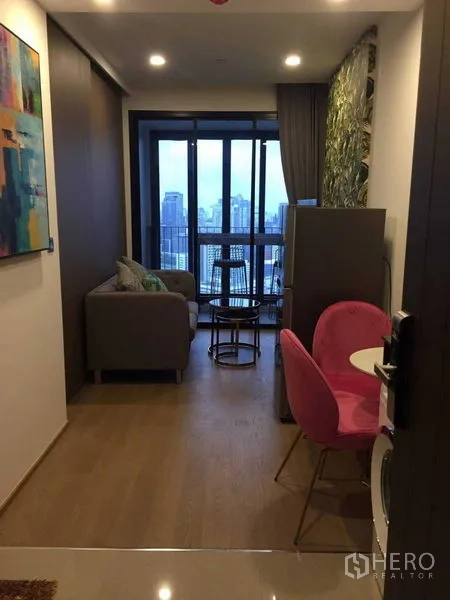 Condominium for rent in Bang Rak, Bangkok - Compact living room with sofa, pink dining chairs and floor-to-ceiling windows opening to a city-view balcony.
