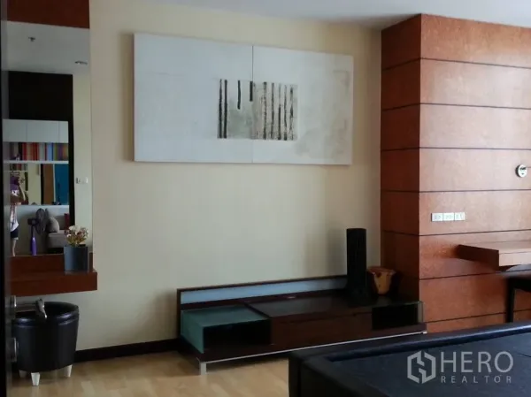 Condominium for rent in Khlong San, Bangkok - Spacious living area with wood panel accent wall, low TV console, wall art and light wood flooring.
