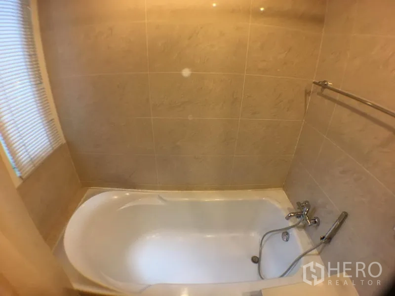 Condominium for rent in Khlong Toei, Bangkok - Tiled bathroom with a full-size bathtub and window blinds.