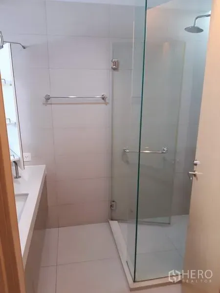 Condominium for rent in Khlong Toei, Bangkok - Clean bathroom with glass-enclosed shower, white tiles, wide vanity and chrome fixtures.