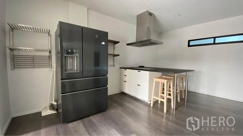 Retail Space for sale in Bang Na, Bangkok - Minimal kitchen with island counter, stools, range hood and large black refrigerator.