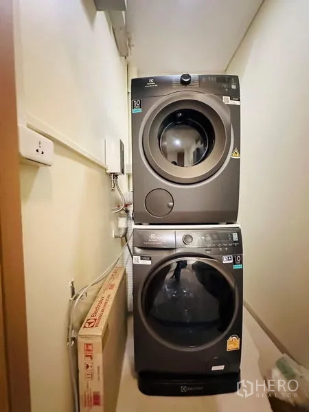 Condominium for rent in Bang Rak, Bangkok - Compact laundry nook with stacked front-loading washer and dryer.