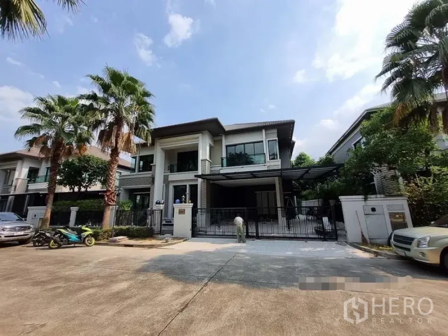 Detached House for rent in Bang Khae, Bangkok - Street view of a gated two-storey detached house with palm trees and driveway.