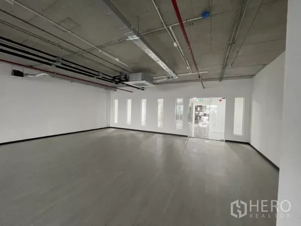 Office Space for rent in Bang Rak, Bangkok - Open office area facing glass entry and slim vertical windows, concrete ceiling with visible piping.