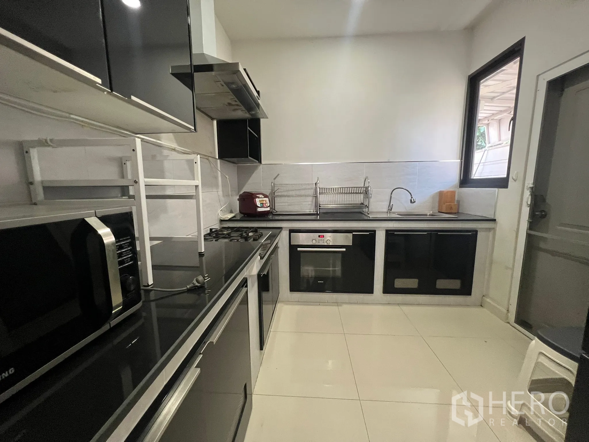 Detached House for rent or sale in Prawet, Bangkok - Fully fitted kitchen with black countertops, gas hob, oven and a window.