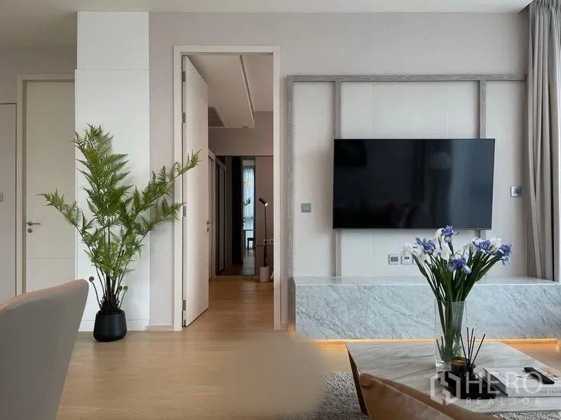 Condominium for rent in Watthana, Bangkok - Living area featuring a large TV wall, indoor plant, and flower arrangement on the coffee table.