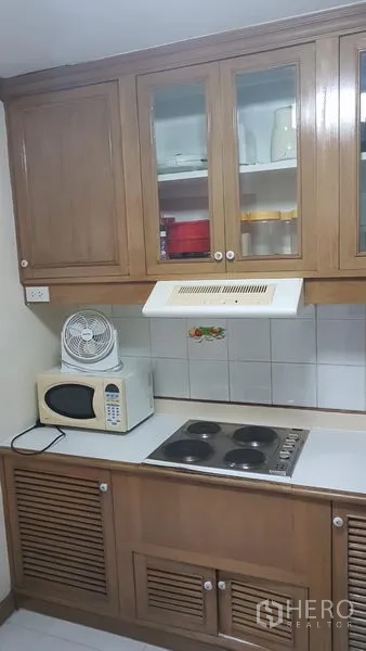 公寓 出租在Watthana, Bangkok - 紧凑厨房，木质橱柜、电灶、微波炉与抽油烟机。