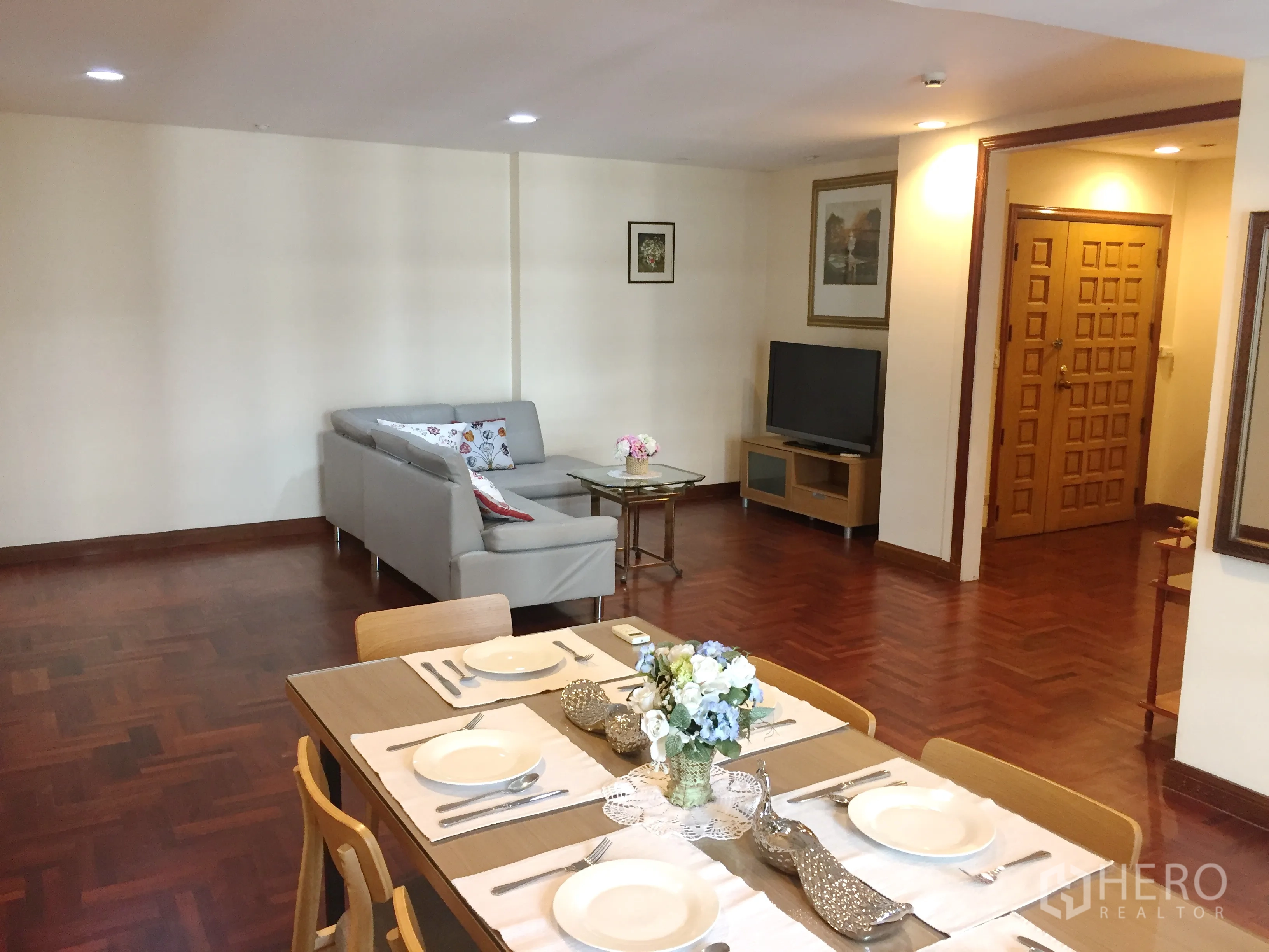 公寓 出租在Pathum Wan, Bangkok - 开放式客餐厅，拼花木地板，灰色沙发、电视柜与木质入户门