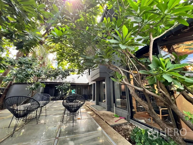 Retail Space for rent in Bangkok - Shaded outdoor terrace with black wire chairs under frangipani trees.