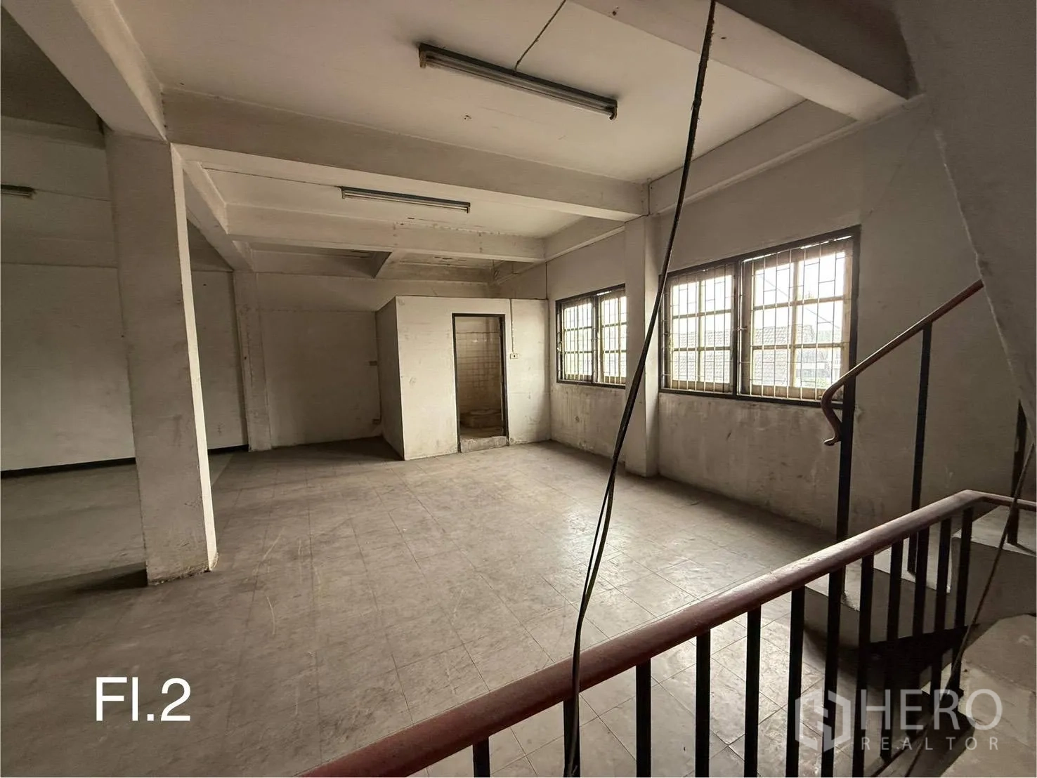 Shophouse for rent in Bang Na, Bangkok - Second-floor open plan room with large barred windows and concrete pillars.
