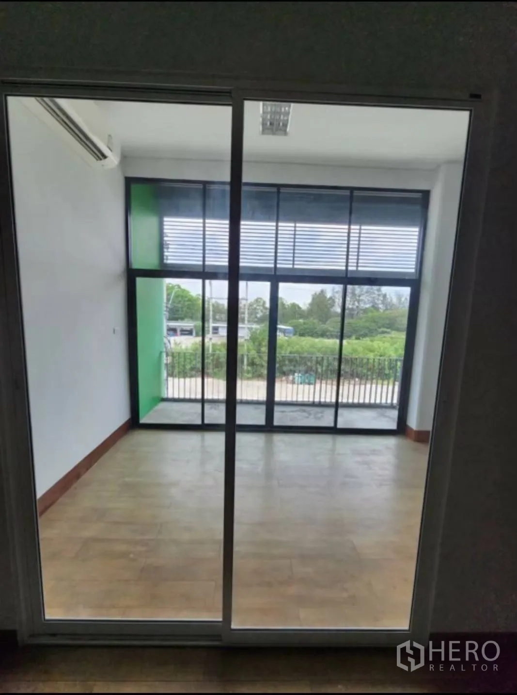 Factory for rent in Samut Prakan - Glass-walled office with sliding door opening to a small balcony and green outlook.