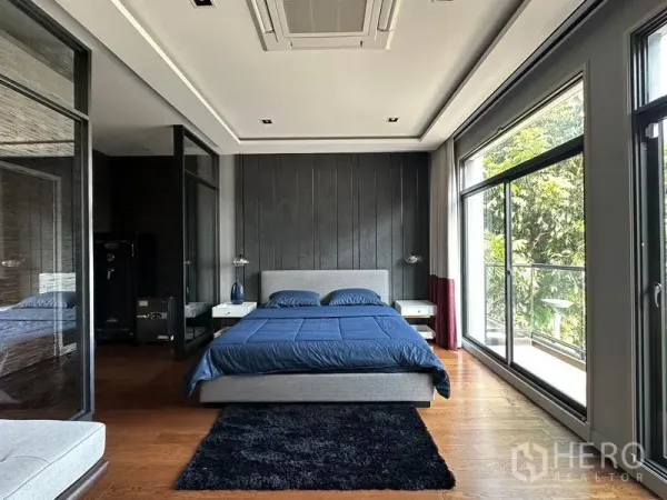 Detached House for rent in Phra Khanong, Bangkok - Spacious master bedroom with floor-to-ceiling windows and balcony overlooking greenery.