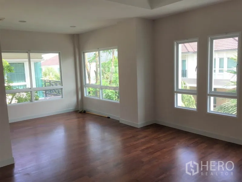 Detached House for rent in Saphan Sung, Bangkok - Corner bedroom featuring wraparound windows with garden views and wooden floors.
