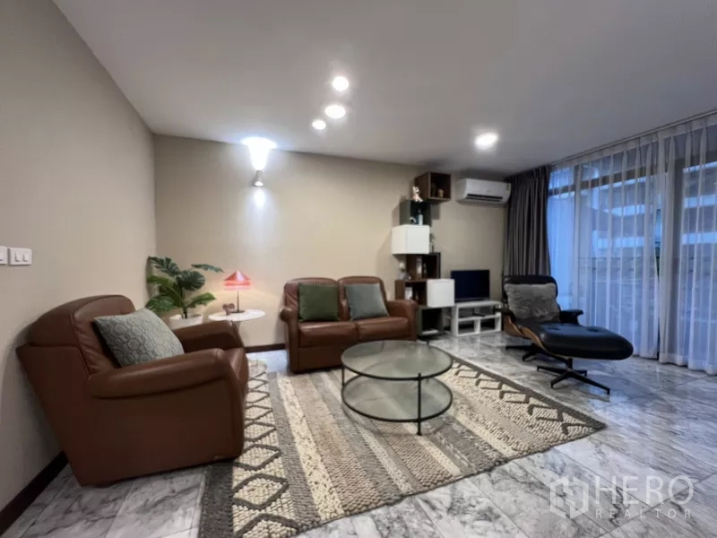 Townhouse for rent or sale in Suan Luang, Bangkok - Cozy lounge with leather sofas, area rug and media unit beside floor‑to‑ceiling windows.