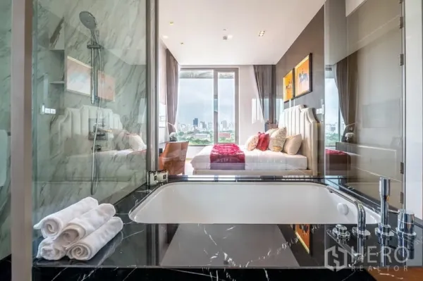 Condominium for rent or sale in Bang Rak, Bangkok - Marble bathroom with glass partition, deep soaking tub and rainfall shower looking toward the bedroom and skyline.
