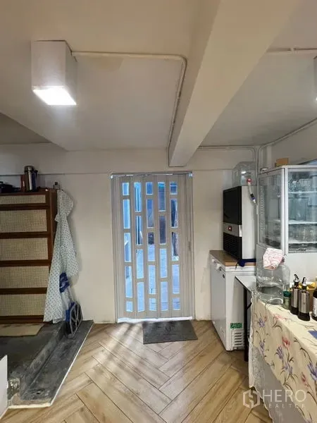 Shophouse for rent in Phra Khanong, Bangkok - Ground-floor prep area with sliding gate, refrigerators and wood-look herringbone floor.