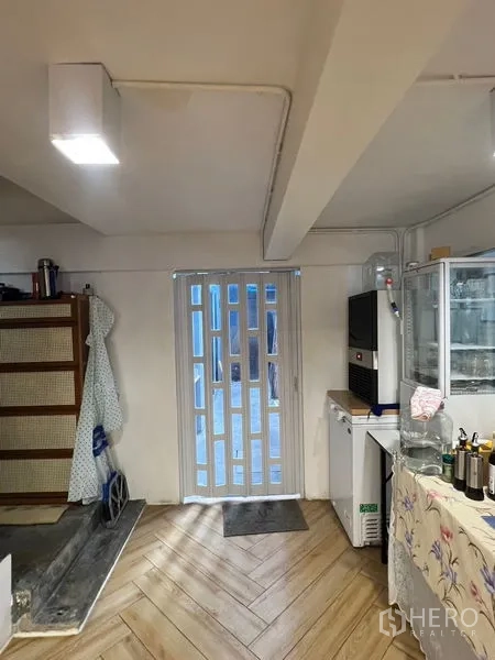Shophouse for rent in Phra Khanong, Bangkok - Ground-floor prep area with sliding gate, refrigerators and wood-look herringbone floor.