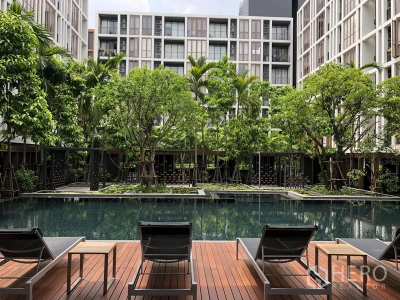 Condominium for rent in Watthana, Bangkok - Resort‑style courtyard swimming pool surrounded by mature trees and sun loungers on a wooden deck.
