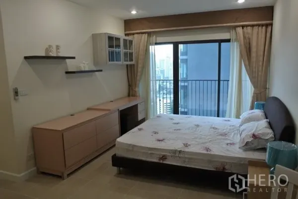 Condominium for rent in Khlong Toei, Bangkok - Spacious master bedroom with desk, built-in storage and balcony with skyline view.