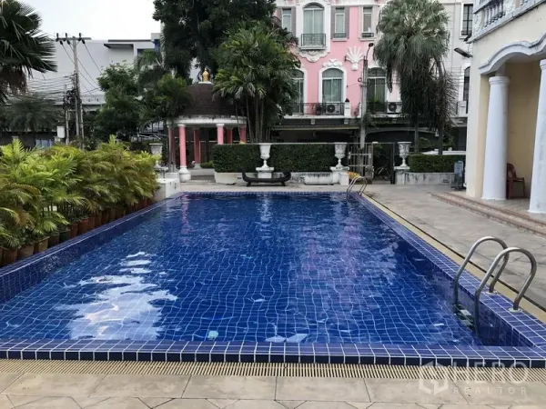 联排别墅 出租在Wang Thonglang, Bangkok - 社区室外公共泳池，蓝色马赛克池面，配金属扶梯与棕榈景观。