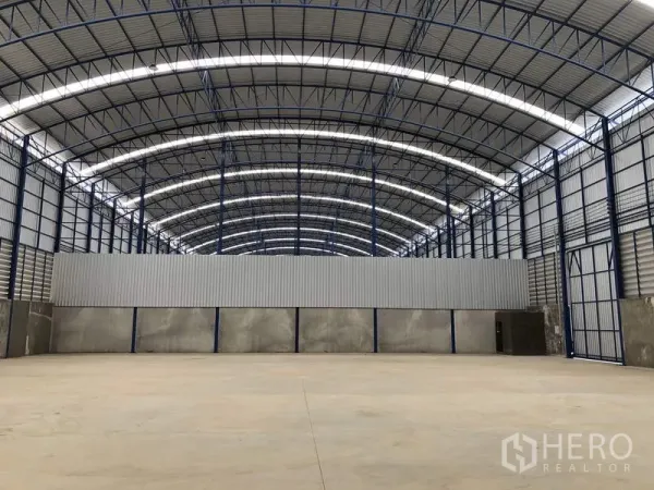 Factory for rent in Lat Lum Kaeo, Pathum Thani - Clear-span warehouse hall with curved roof trusses and a partial partition wall.
