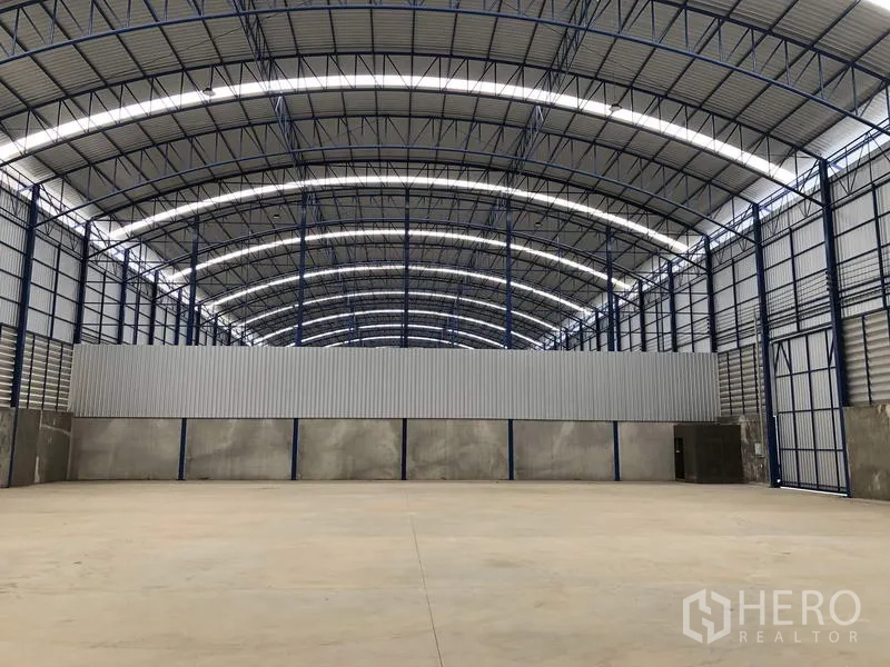 Factory for rent in Lat Lum Kaeo, Pathum Thani - Clear-span warehouse hall with curved roof trusses and a partial partition wall.