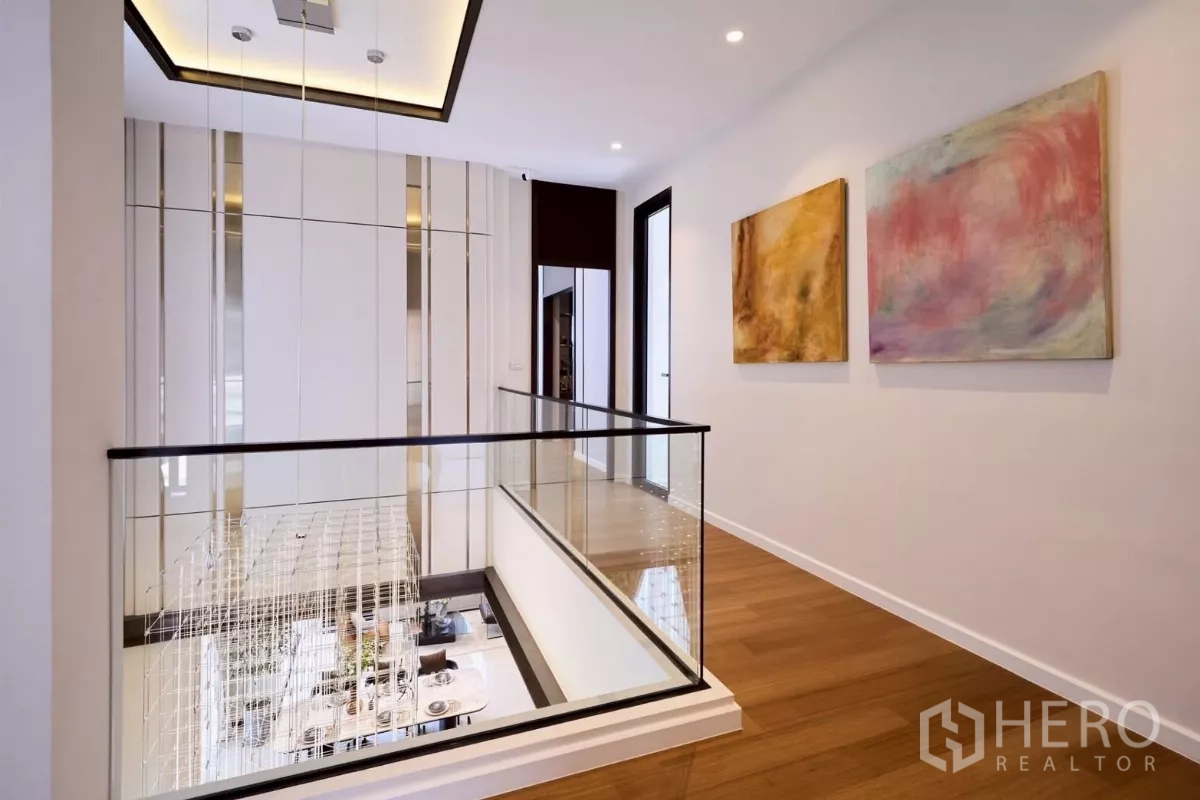 Detached House for sale in Lat Phrao, Bangkok - Upper hallway with glass balustrade overlooking chandelier and living area below.