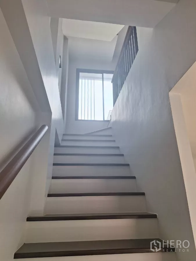 Townhouse for rent in Mueang Samut Prakan, Samut Prakan - White staircase leading to a landing with a large window for natural light.