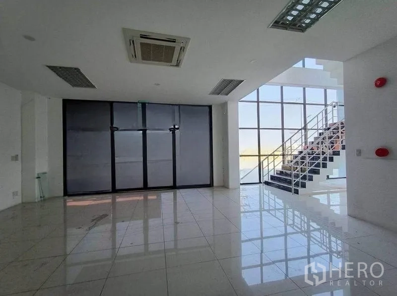 Warehouse for rent or sale in Pathum Thani - Bright lobby with floor-to-ceiling windows, tiled floors, and a glass stairway.
