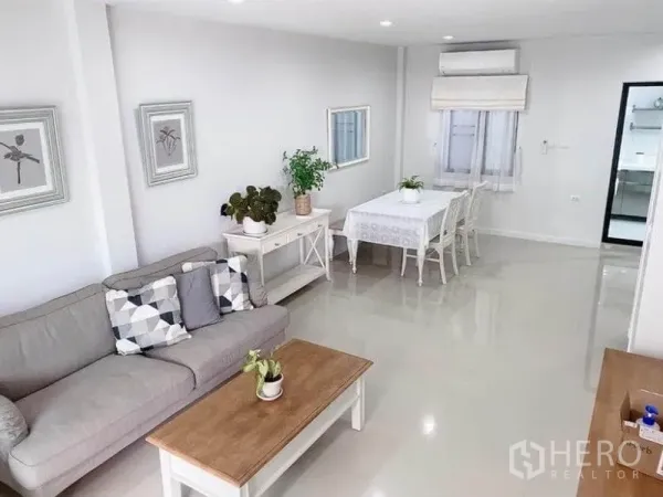 联排别墅 出租在Prawet, Bangkok - 明亮的客餐厅一体空间，灰色沙发、白色餐桌、筒灯与亮面地砖。