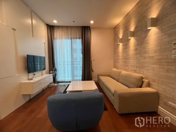 Condominium for rent in Khlong Toei, Bangkok - Living area with brick accent wall, sofa, coffee table and access to the balcony.