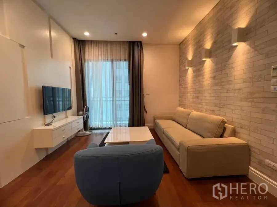 Condominium for rent in Khlong Toei, Bangkok - Living area with brick accent wall, sofa, coffee table and access to the balcony.