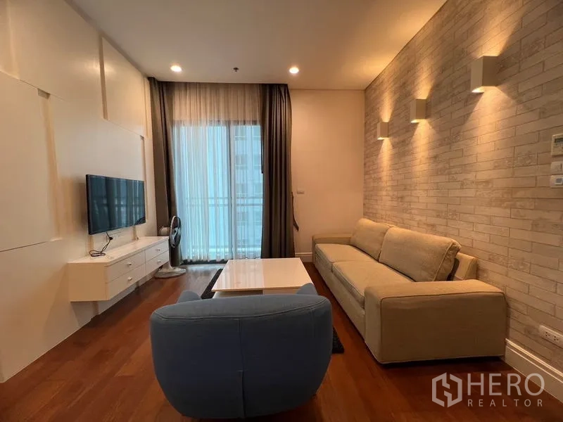 Condominium for rent in Khlong Toei, Bangkok - Living area with brick accent wall, sofa, coffee table and access to the balcony.