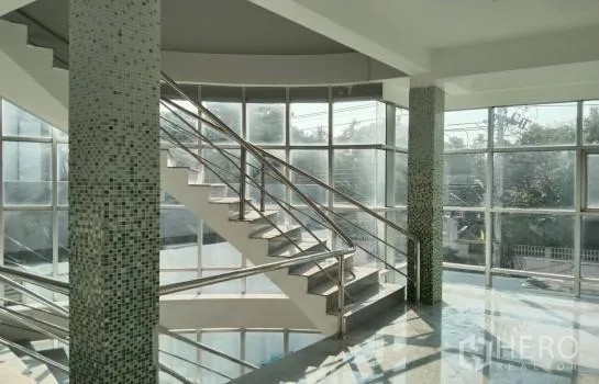 Warehouse for rent or sale in Prawet, Bangkok - Sunlit atrium featuring a curved staircase and floor-to-ceiling windows.