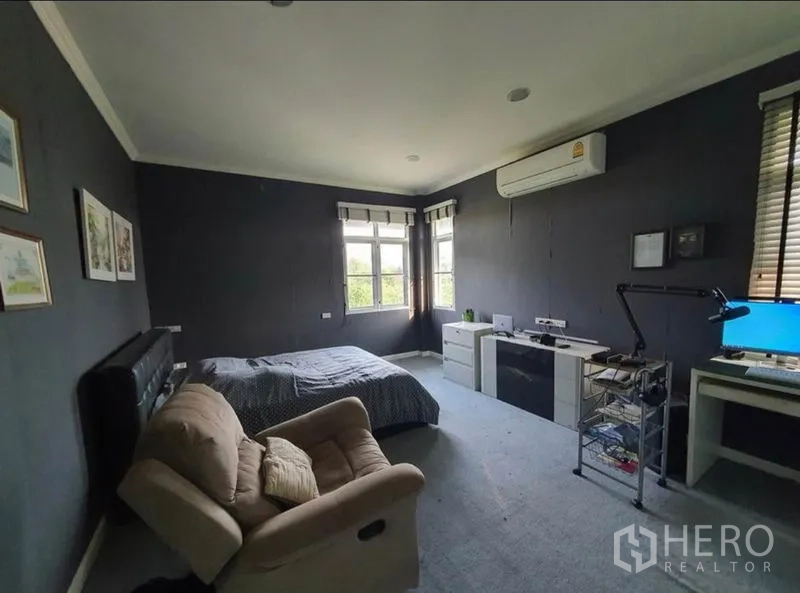 Detached House for sale in Sai Mai, Bangkok - Spacious bedroom with desk setup, dark accent walls, large windows and air conditioner.